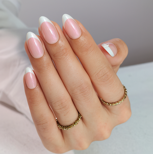 Hand with pink and white nail polish wearing gold rings on a neutral background